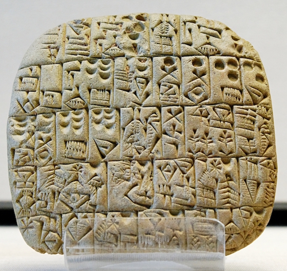 A photograph of an ancient Sumerian clay tablet with cuneiform writing showing a sales contract for a house and field.